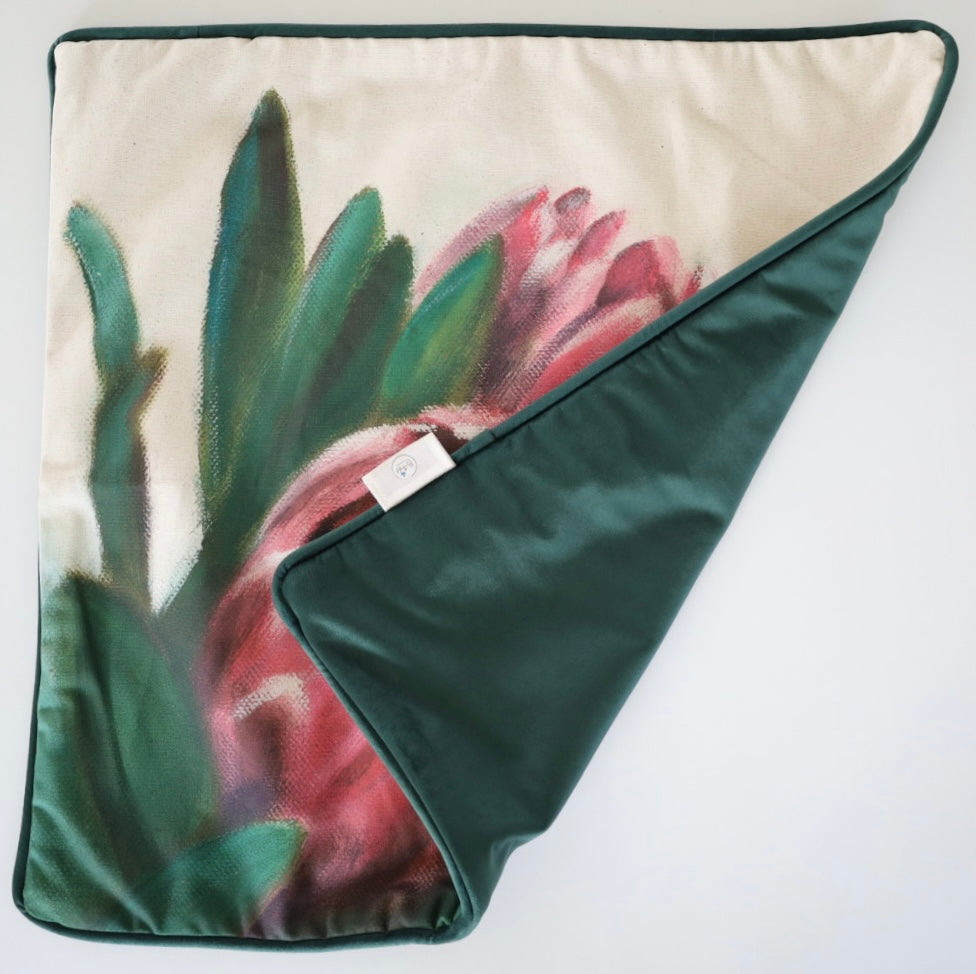 Image shows folded back and front of square 60×60 cm cushion cover with pink proteas from oil painting print, velvet piping, velvet back, and concealed zip closure.